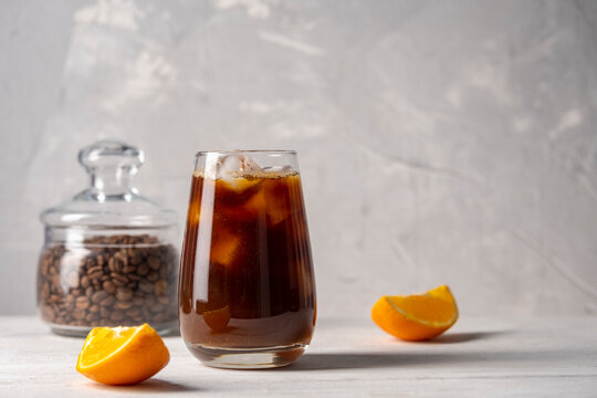 Coffee with orange juice bumble in a tall glass with ice on a light background with coffee beans, fruits and morning shadows