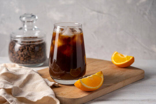 Coffee with orange juice bumble in a tall glass with ice on a light background with coffee beans, fruits and morning shadows