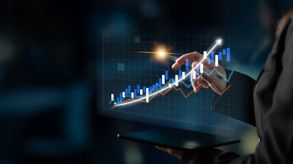 Obraz premium A businesswoman engages with financial data through a laptop, showcasing virtual graphs that indicate market trends and growth opportunities. Impute