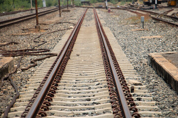 Fototapeta premium Detailed view of parallel steel rails fixed with rusted clips on concrete sleepers. Industrial railway construction texture with gravel ballast and linear perspective.
