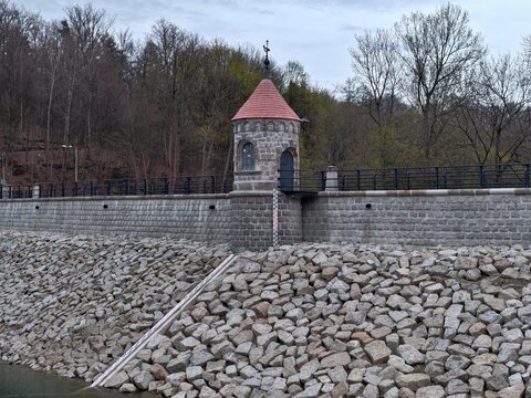 Distant trees and tranquil industrial scene. Gray sky over dam with layered stone revetment and path