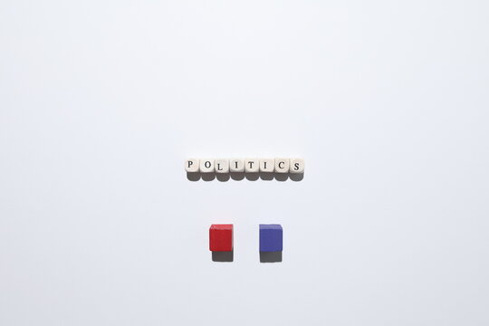 POLITICS spelled with cubes and red and purple blocks representing division, debate and opposing ideologies on white background.