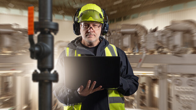 Industrial plant, Technical inspection. Engineer in protective gear checks equipment and pipeline systems with laptop, monitoring production and maintenance processes.
