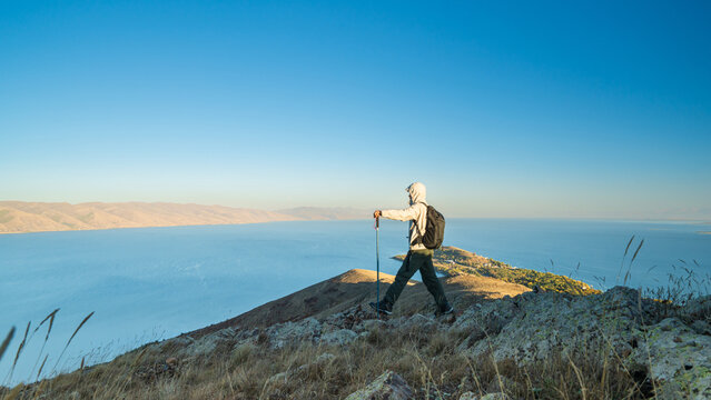 Hiker standing on a mountain ridge during sunrise near Lake Sevan, Armenia, enjoying the beautiful morning light over the calm blue lake.