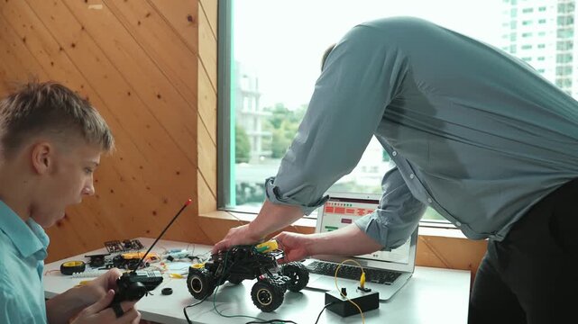 Skilled teacher help young student fixing car model at STEM class. Professional instructor repair robotic machines at table with laptop display programming system and coding prompt. Edification