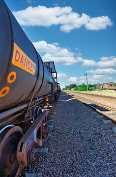 Industrial Fuel Tanker Train with Danger Sign on Railway Tracks tracks receding toward a bright, cloudy horizon.