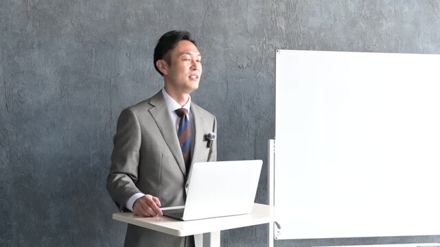 グレー背景でプレゼンをするスーツを着た日本人男性