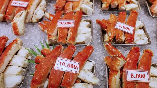 Assortment of fresh king crab legs displayed on ice with price tags at a seafood market.