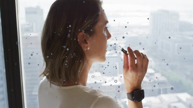 Businesswoman at high-rise window, overlay appearing, touching pen to lips, planning city strategy