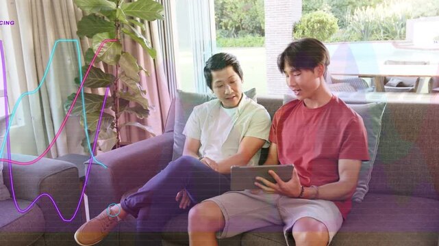 Father and son sitting on sofa, teen tapping tablet initiating waveform overlays, testing home tech