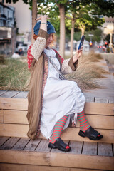 Obraz premium Stylish young red-haired woman sitting outdoors and using a smartphone. Fashionable female in casual modern outfit enjoying mobile technology in an urban environment. Concept of communication, social 