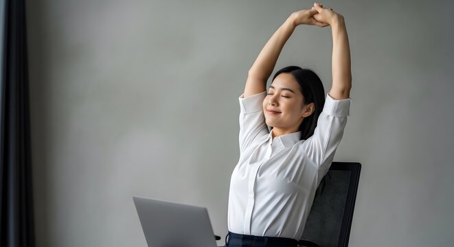 Asian businesswoman stretching her arms while working at desk in office