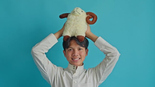 Happy Muslim teenager holding stuffed ram doll on top of head for symbolizing joyful and lighthearted Qurban celebration