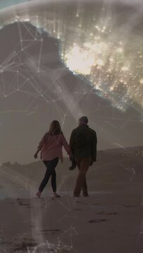 Vertical video: Couple walking beach together, tech overlay intensifying and bathing them in gold