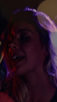 Vertical video: Female singer raising mic, starting singing for music as bokeh drifts across face
