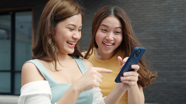 Young Gen Z asia people trending influencer teen girl look at phone enjoy read review and watch viral video laugh joy play social media app post share online fun standing in modern city relax outside.
