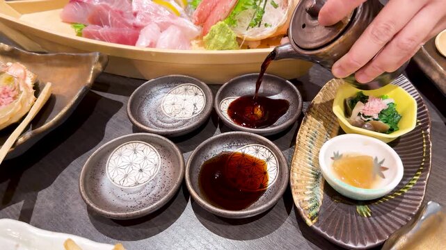 Pouring dark soy sauce into ceramic dishes for japanese sashimi dinner in luxury restaurant setting.
