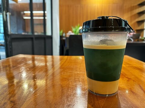 Iced coffee drink in a plastic cup with black lid on a wooden table at a cafe. Refreshing cold brew or latte for modern lifestyle, beverage retail, and coffee shop culture concepts.