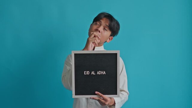 Muslim teenager presenting "EID AL ADHA" message board shifting from thinking pose to inspired look while gesturing toward top 