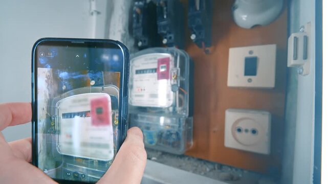 Hand Holding Smartphone and Taking Photo of Electric Meter Readings | Tracking Home Electricity Consumption and Utility Bills | Residential Energy Monitoring Concept