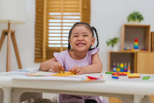 happy preschool child girl drawing and painting with colorful oil pastels on paper