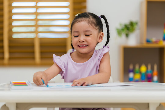 happy preschool child girl drawing and painting with colorful oil pastels on paper