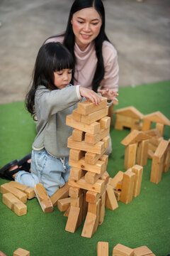 mother and preschool child girl playing with wooden toy block at outdoor