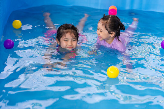 happy preschool child girl playing together with her sister in outdoor portable swimming pool in backyard