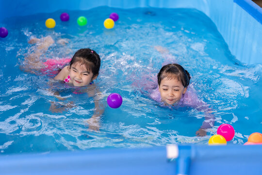 happy preschool child girl playing together with her sister in outdoor portable swimming pool in backyard