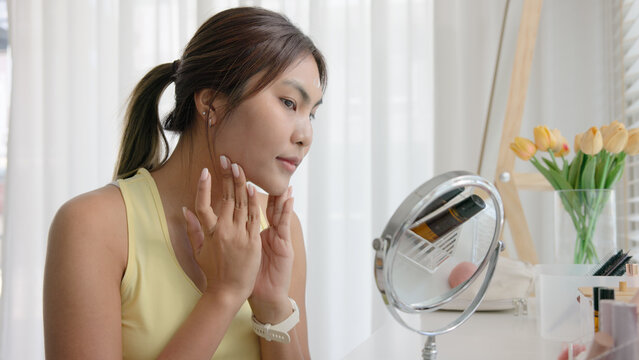 Young adult woman gen z black asia people relax get ready prepare clean makeup apply cream skin care make up getting dressed at home. Look at mirror camera self love anti aging health happy vanity.