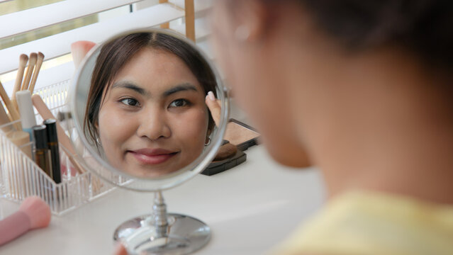 Young adult woman gen z black asia people relax get ready prepare clean makeup apply cream skin care make up getting dressed at home. Look at mirror camera self love anti aging health happy vanity.