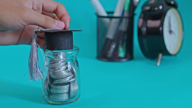 High-angle shot of student&rsquo;s hand crowning coin jar with graduation hat