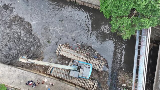 An blue excavator is working to digging the bottom of the jakarta river, Excavator with a long arm.  floating platform in a river digging cumulative dirt that shallowing the river