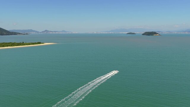 Aerial shot of jet ski speeding across calm waters at Praia da Daniela leaving a long white wake, Florianopolis.