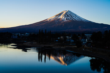 Fototapeta premium Stunning sunrise reflection of snow-capped Mount Fuji on the calm water of Lake Kawaguchiko in Japan. 