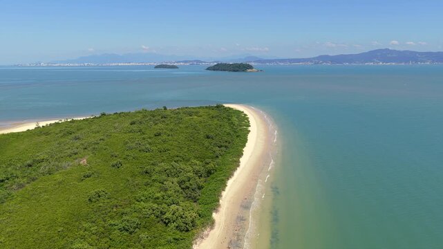 Aerial forward shot advancing over Praia da Daniela peninsula with dense greenery and surrounding blue ocean.