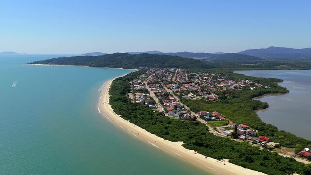 Praia da Daniela in Florian&oacute;polis Santa Catarina Brazil on Atlantic Ocean with narrow peninsula, calm bay waters, and lagoon behind backed by Serra do Mar, aerial glide