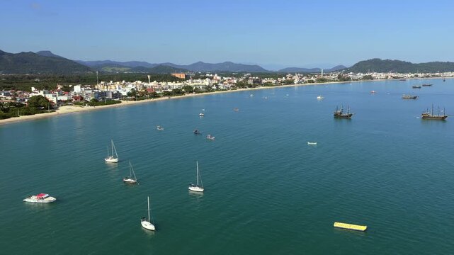 Cachoeira do Bom Jesus and Canasvieiras in Florian&oacute;polis Santa Catarina Brazil on Atlantic Ocean with wide bay, sailboats, and coastal town extending along shoreline toward Serra do Mar, drone forward