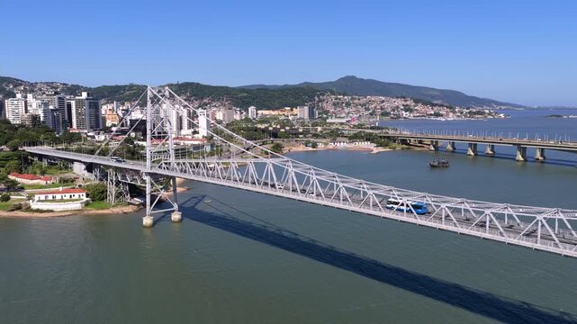 Ponte Hercilio Luz in Florianopolis Santa Catarina Brazil extending over Baia Norte with Centro and Estreito connection alongside Pedro Ivo Campos Bridge and urban skyline, drone pullback shot