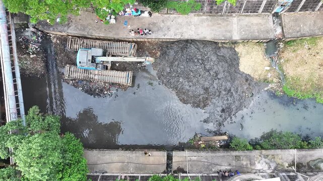 Aerial View An blue excavator is working to digging the bottom of the jakarta river, Excavator with a long arm.  floating platform in a river digging cumulative dirt that shallowing the river