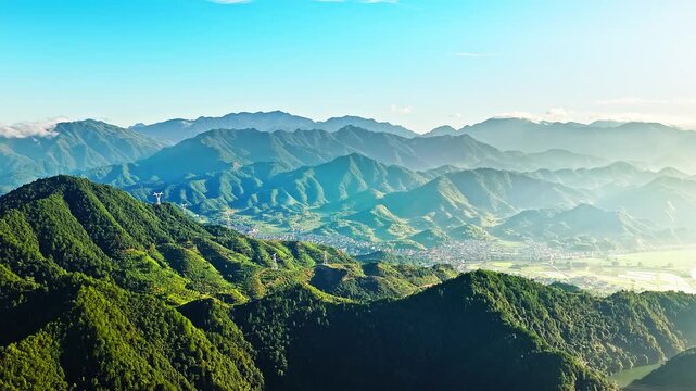 Aerial view of lush green mountain ranges and a rural valley village under a clear blue sky in Jiangxi, China