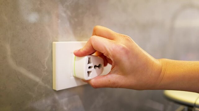 Close Up of Hand Unplugging Universal Travel Adapter From Wall Outlet