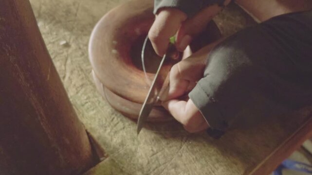 Close up of hands preparing fishing line and hook on a wooden surface in a rural coastal village. Warm natural light highlights traditional fishing preparation activity in a tropical environment.
