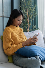 Obraz premium Asian woman sit on sofa using smartphone in living room