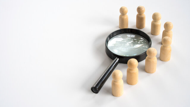 Magnifying glass focused on a group of wooden people for recruitment and human resources investigation concept.