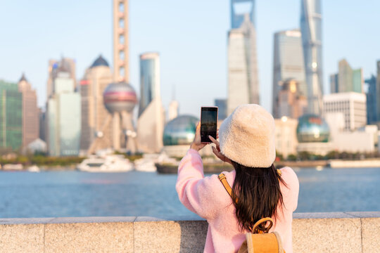 Female tourist taking a photo and enjoying the view of Shanghai skyline with a smartphone at The Bund, China