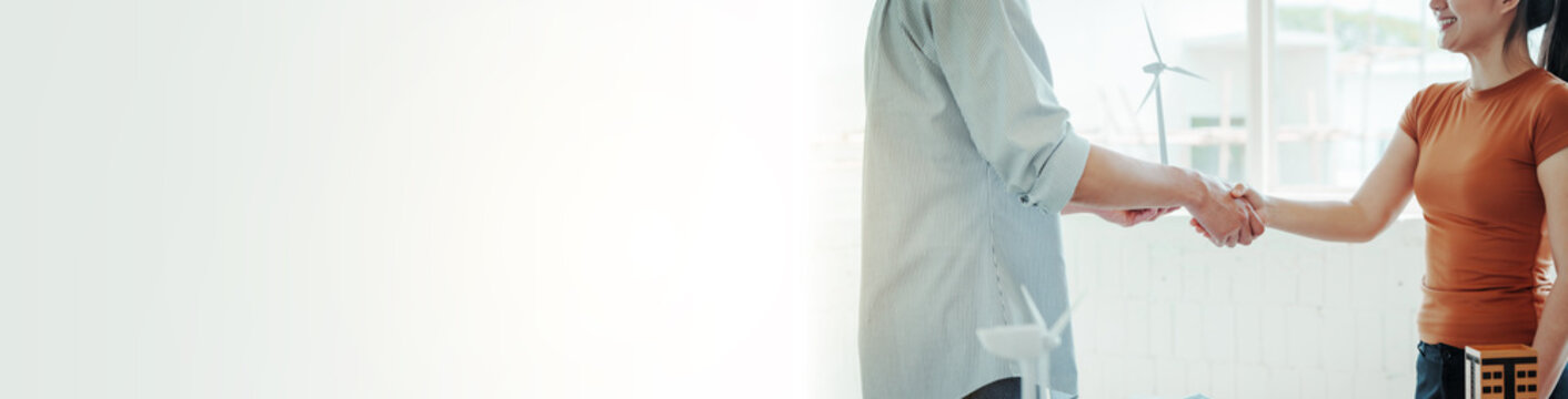 Business partners shaking hands in bright office, with wind turbine models and sustainable energy concept, showing clean power collaboration and agreement.