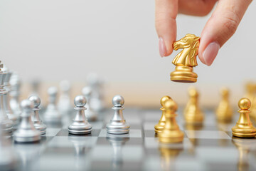 hand moving gold Chess knight figure and Checkmate opponent during chessboard competition. Strategy, Success, management, business planning, win, disruption, Trade war and leadership concept © Jo Panuwat D