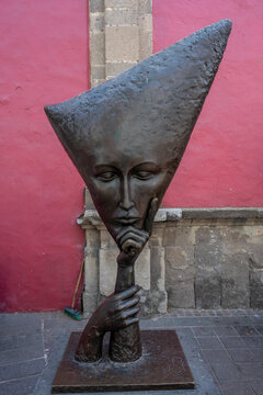 Tlaquepaque, Mexico - March 14 2026: Modern bronze sculpture depicting a pensive face with a unique elongated head shape, captured in Tlaquepaque, Jalisco, Mexico's vibrant art district. Against a bri