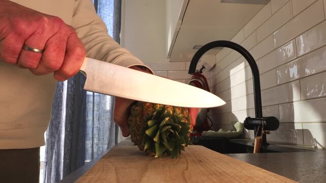 Stockholm, Sweden A cook slice a pineapple on a cutting board. 